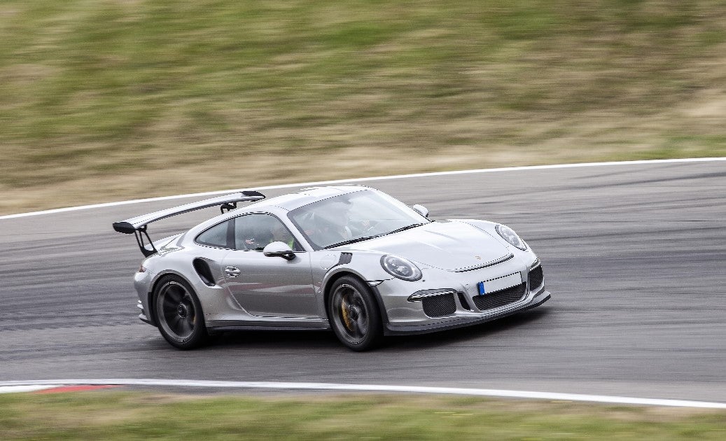 Silver metallic Porsche 911 GT3 RS 991 equipped with Öhlins suspension driving fast on a racetrack.