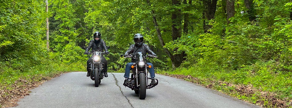 Two motorcycles equipped with Öhlins suspension riding on a road in the woods.