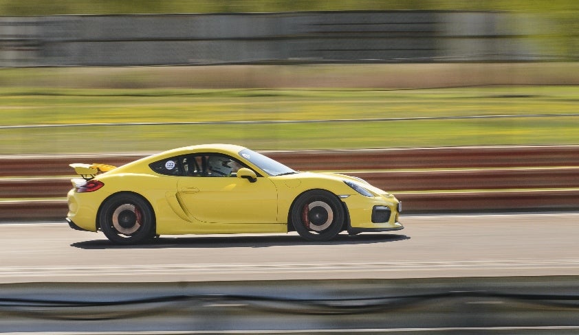 Yellow Porsche 718 Cayman GT4 981 equipped with Öhlins suspension side view driving fast on a racetrack.