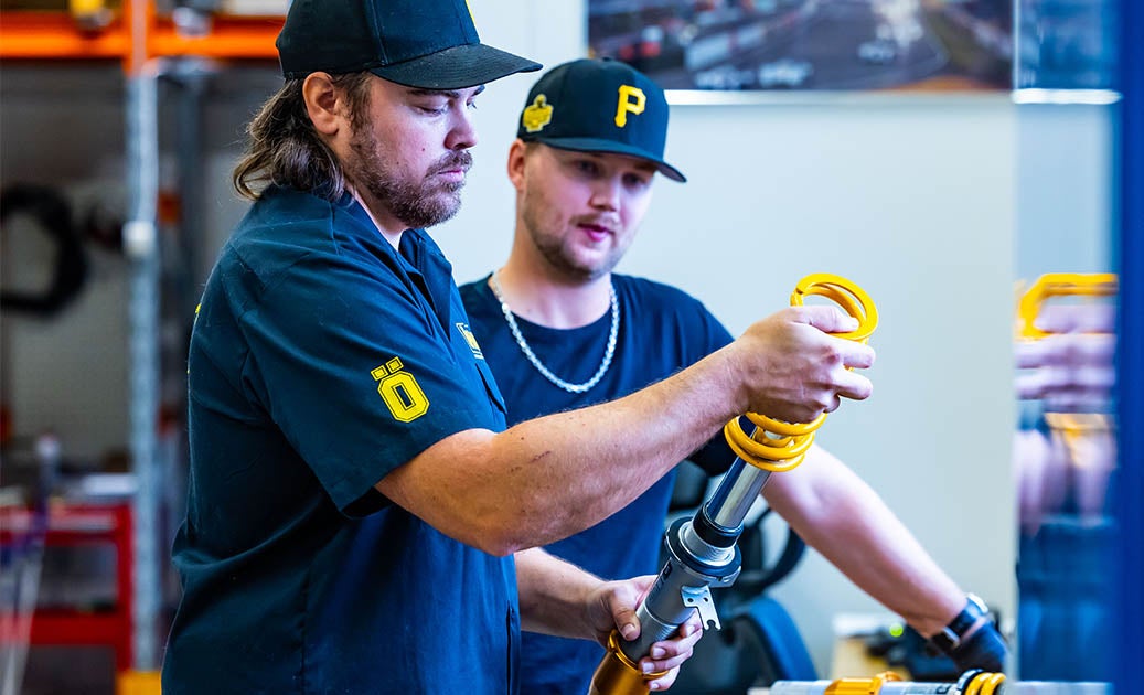Two Öhlins employees in blue shirts assembling suspension in the factory.